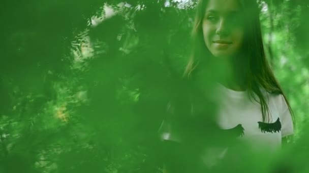 Κομψό κορίτσι στο καταπράσινο δάσος ποζάρει πίσω από τα φύλλα — Αρχείο Βίντεο