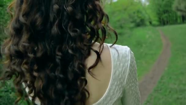 Брюнетка с вьющимися волосами в белом платье ходит по тропинке — стоковое видео