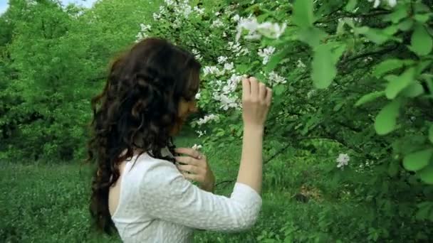 Morena bonita com cabelo encaracolado cheira a flores em um parque — Vídeo de Stock