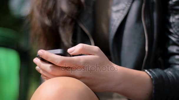 Morena se sienta al aire libre en un banco y mirando el teléfono móvil — Vídeos de Stock