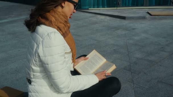 Молодая симпатичная девушка в очках читает книгу — стоковое видео