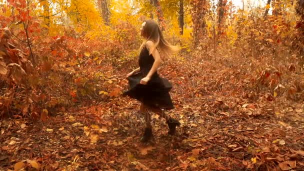 Chica joven en vestido negro girando en el bosque de otoño — Vídeos de Stock