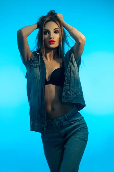 Joven hermosa chica con labios rojos en ropa de mezclilla posando en la cámara sobre fondo azul — Foto de Stock