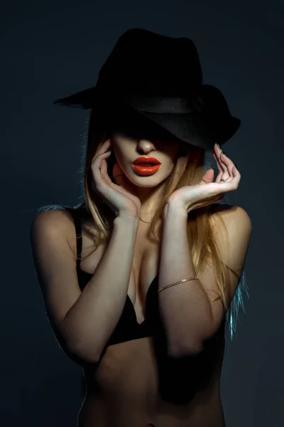 Portrait of slim young girl in black bra with red lips wearing a hat with wide brim in studio — Stock Photo, Image