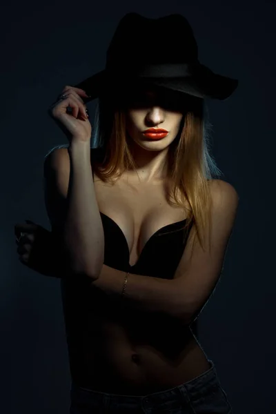 Ritratto di giovane ragazza in reggiseno nero con labbra rosse che indossa un cappello con ala larga in studio — Foto Stock