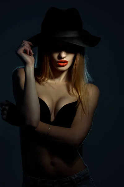Νεαρή κοπέλα σε μαύρο σουτιέν με κόκκινα χείλη που φοράει ένα καπέλο με ευρύ γείσο στο studio — Φωτογραφία Αρχείου