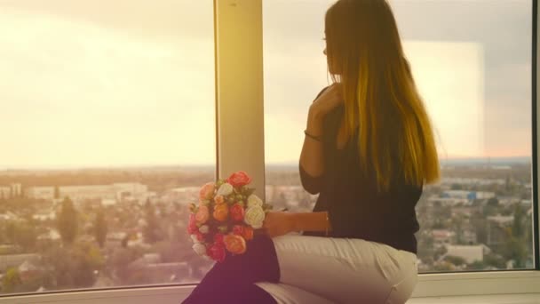 Menina bonita olha para a grande janela e flores cheirosas — Vídeo de Stock