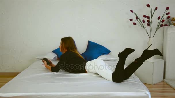 Slender girl lies in boots on the bed and makes a photo — Stock Video