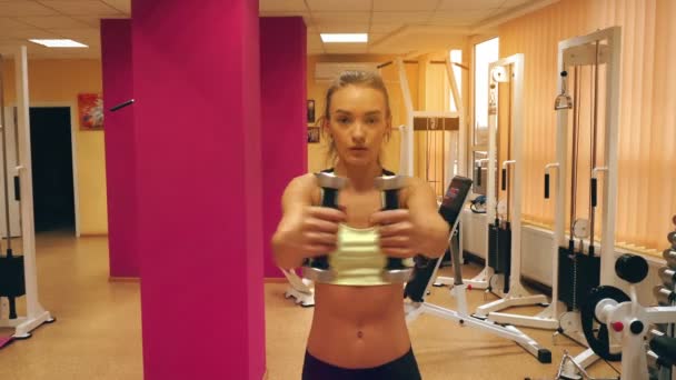 Mujer rubia concetrada trabajando duro en un gimnasio con pesas — Vídeo de stock