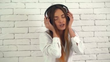 4 k Beyaz tuğla duvar arka planda müzik kulaklık ile eğlenceli ve dinleme ti sahip genç kız portresi