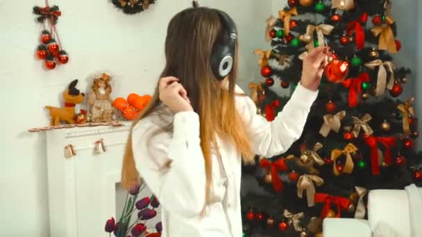Komik kız kulaklık ile müzik dinler ve bir Noel ağacı süsle — Stok video