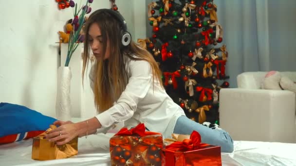 Flicka lyssnar på musik med hörlurar med en massa julklappar på sängen — Stockvideo
