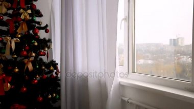 güzel genç sarışın siyah bir gömlek ve Noel ağacı yakınındaki penceresine yürüyen çorap perdeler açılır ve Merhaba jest