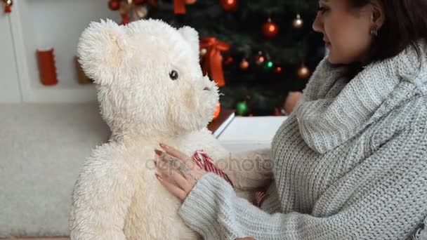 かわいい若い女の子クリスマス ツリーのそばに座って 大きなおもちゃのクマを家庭で保持 — ストック動画