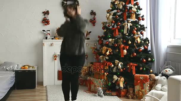 短い髪の若い女性がクリスマス ツリーを自宅近くのヘッドフォンで音楽を聴く — ストック動画