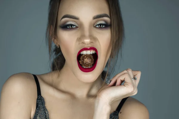 Ung flicka med röda läppar äter choklad godis och tittar på den — Stockfoto