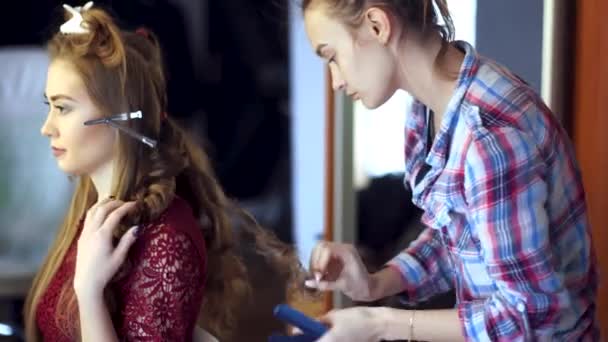 Blonde stylist girl makes hairstyle to a young woman — Stock Video