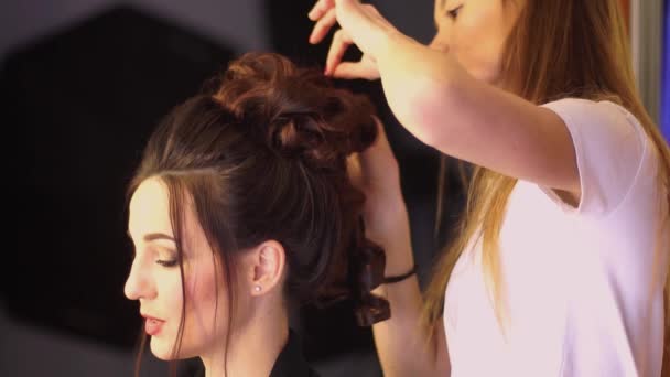 Jovem menina estilista loira faz penteado para uma mulher — Vídeo de Stock
