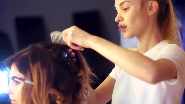Молода дівчина-стилістка робить зачіску для дами — стокове відео
