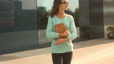 Genç şirin esmer gözlük ile sokakta yürürken elinde kitaplar