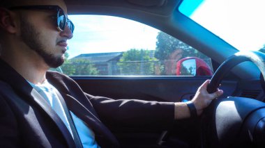 Siyah güneş gözlüklü seksi bir genç adam araba kullanıyor.