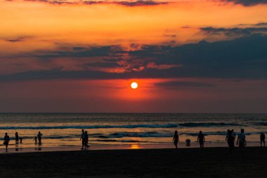Bali, Endonezya - 11 Ekim 2015: Endonezya 'nın Bali adasında gün batımı. İnsanlar sahilde yürür..