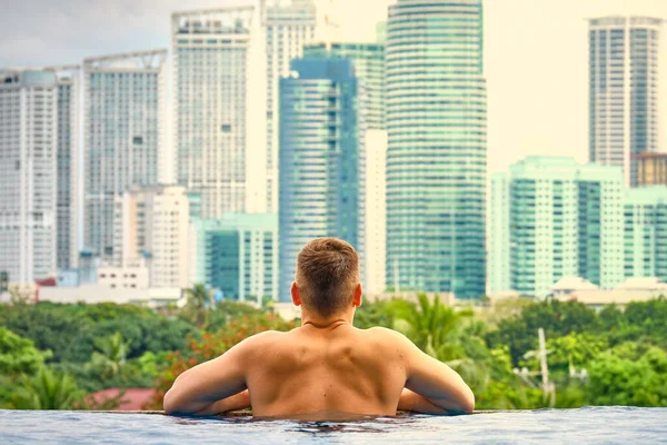 A man in the pool on the roof of the hotel. View of the city of Manila from the pool of the luxury five-star Discovery Primea hotel. Sunny weather. Skyscrapers on the background.