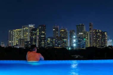Beş yıldızlı lüks Discovery Primea otelinin havuzundan Manila 'nın gece manzarası. Güneşli bir hava. Arka planda gökdelenler.