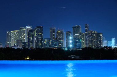Beş yıldızlı lüks Discovery Primea otelinin havuzundan Manila 'nın gece manzarası. Güneşli bir hava. Arka planda gökdelenler.
