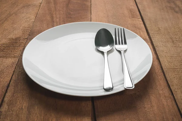 Spoon and fork in white plate on wooden table — Stock Photo, Image