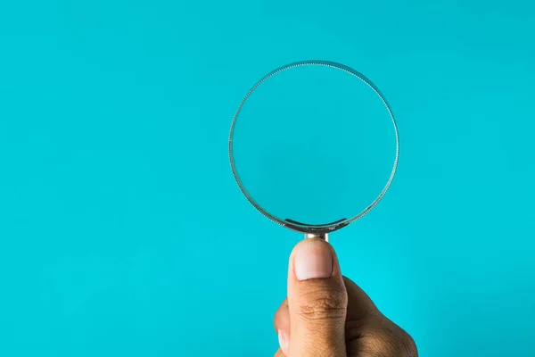 Iemands hand met vergrootglas met blauwe achtergrond. — Stockfoto