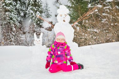 Karlı kış yürüyüş bir kardan adam ile mutlu güzel çocuk kız plaing. Çocuk bina kardan adam, Xmas.