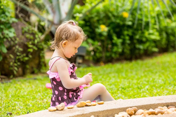 Linda niña en traje de baño jugando con piedras en una playa de guijarros —  Fotos de Stock