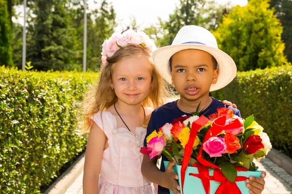 Schwarzafrikanisch-amerikanisches Junge-Kind schenkt Mädchen zum Geburtstag Blumen. kleine entzückende Kinder im Park. Kindheit und Liebe. — Stockfoto
