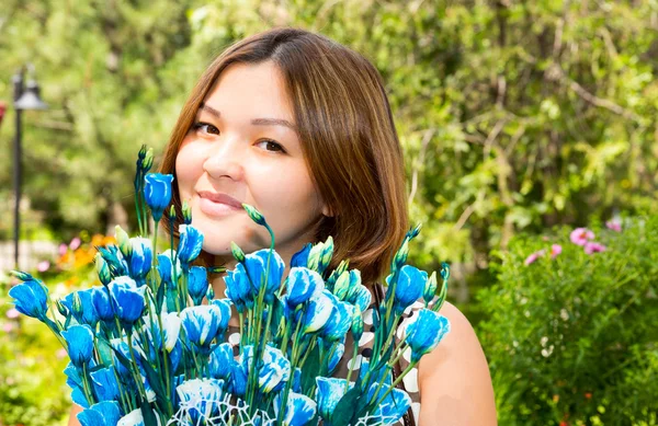 Porträtt av den asiatiska Kazakiska unga vackra leende kvinna och blommor utomhus — Stockfoto