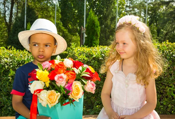 Schwarzafrikanisch-amerikanisches Junge-Kind schenkt Mädchen zum Geburtstag Blumen. kleine entzückende Kinder im Park. Kindheit und Liebe. — Stockfoto