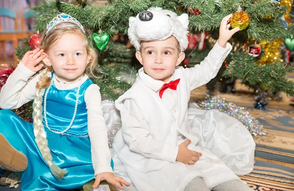 Two children dressed in carnival suits near christmas fir tree in New Year's children's holiday with gifts — Stock Photo, Image