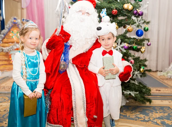 Dvě děti oblečené v karnevalové obleky s Santa Claus poblíž vánoční jedle v novoroční děti dovolenou s dárky — Stock fotografie