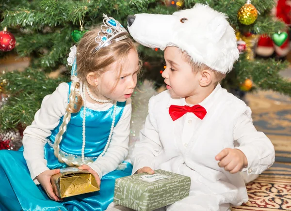 Twee kinderen gekleed in carnaval kostuums in de buurt van Spar kerstboom in New Year's Kinder vakantie met geschenken — Stockfoto