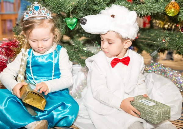 Two children dressed in carnival suits near christmas fir tree in New Year's children's holiday with gifts — Stock Photo, Image