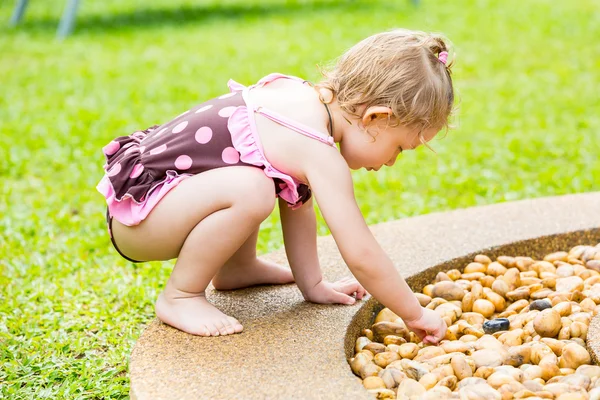 Cute little child girl in a swimsuit playing with stones on a pebble beach — Stock Photo, Image
