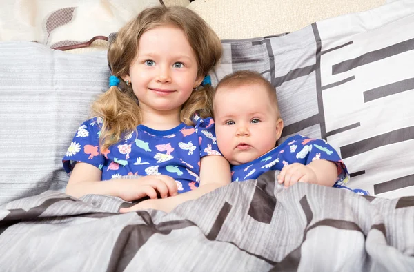 Twee zussen. Oudere zus kid knuffelen zijn pasgeboren zusje. Schattige kinderen meisjes op bed thuis. — Stockfoto