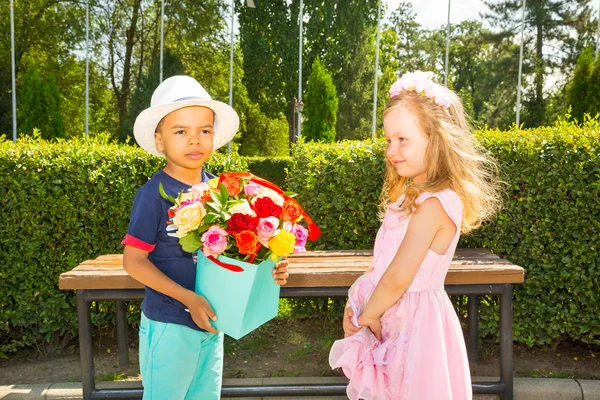 Schwarzafrikanisch-amerikanisches Junge-Kind schenkt Mädchen zum Geburtstag Blumen. kleine entzückende Kinder im Park. Kindheit und Liebe. — Stockfoto