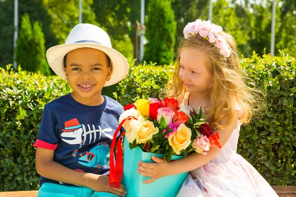 Black african american boy kid gives flowers to girl child on birthday. Little adorable children in park. Childhood and love. — Stock Photo, Image