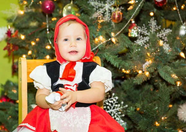 Portrait of girl child in suit a red hat for Christmas around a fir-tree decorated. Kid on holiday new year — Stock Photo, Image