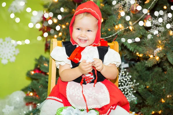 Portrait of girl child in suit a red hat for Christmas around a fir-tree decorated. Kid on holiday new year — Stock Photo, Image