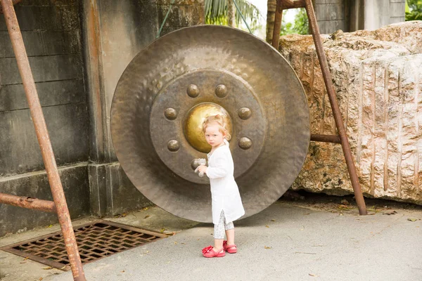 Kind in de buurt van Thaise gong in Phuket. Traditie Aziatische bell in Boeddhisme tempel in Thailand. Beroemde grote bell wens in de buurt van gouden Boeddha — Stockfoto