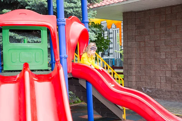 Szczęśliwy Urocza dziewczyna na slajdów dla dzieci na plac zabaw w pobliżu Przedszkole montessori w letni dzień — Zdjęcie stockowe