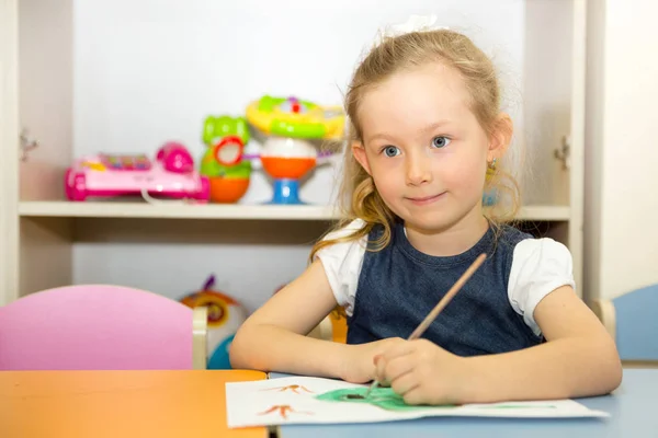 Schattig kind meisje een penseel tekent en schildert in kwekerij kamer. Kind in de kleuterschool in Montessori preschool klasse. — Stockfoto