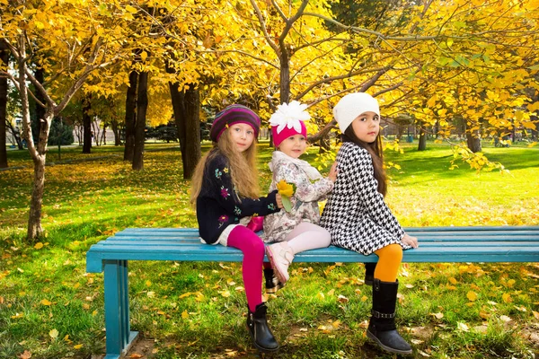 Осенний портрет красивых детей на скамейке. Счастливые маленькие девочки с листьями в парке осенью . — стоковое фото